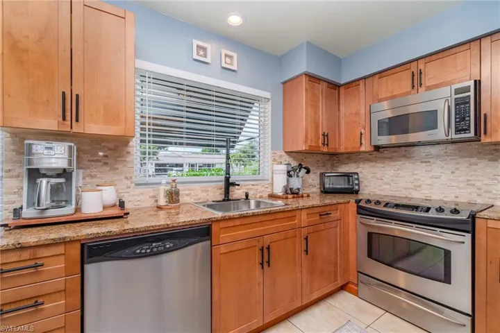 Kitchen with stainless steel appliances, light stone countertops, sink, and light tile patterned floors
