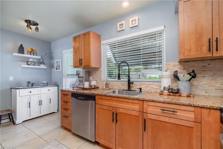 Kitchen featuring sink, tasteful backsplash, light tile patterned floors, stainless steel dishwasher, and light stone countertops