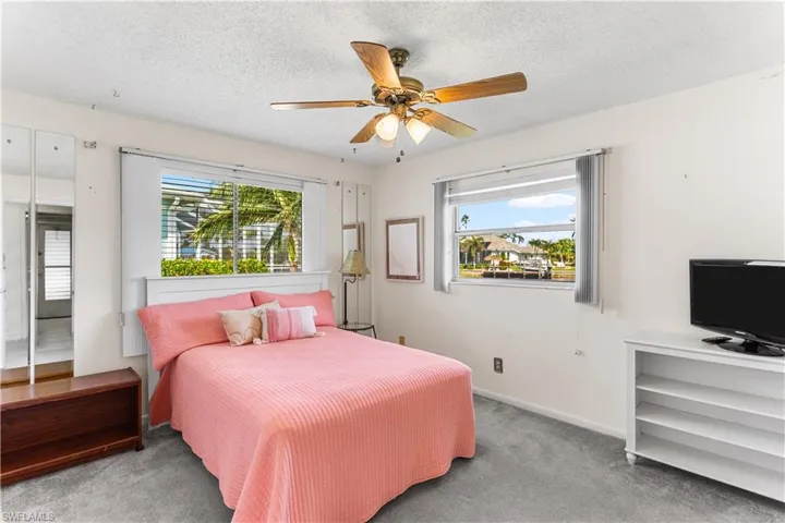 Carpeted bedroom with ceiling fan, multiple windows, and a textured ceiling