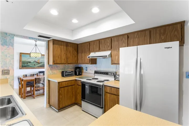 Kitchen featuring backsplash, white appliances, a raised ceiling, and decorative light fixtures
