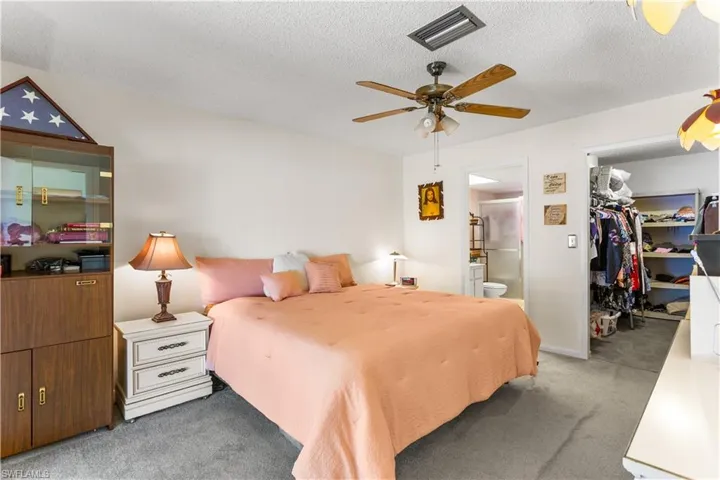 Carpeted bedroom with ensuite bathroom, ceiling fan, a textured ceiling, a walk in closet, and a closet