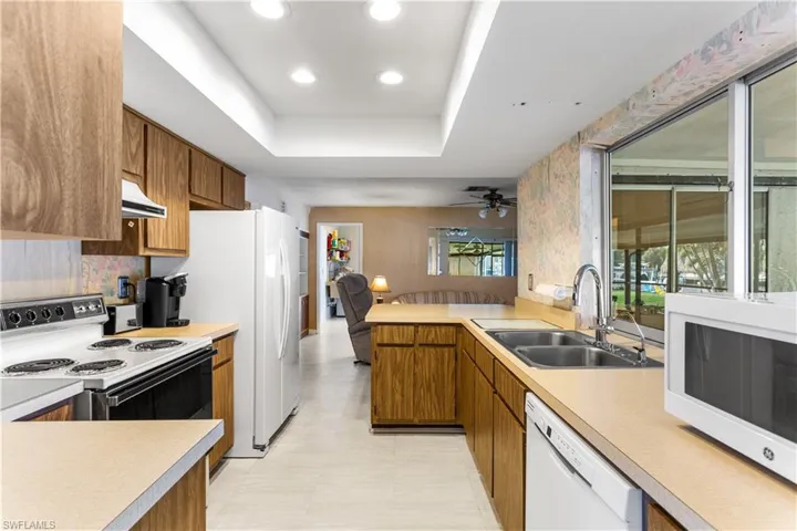 Kitchen featuring sink, ceiling fan, custom exhaust hood, white appliances, and a raised ceiling
