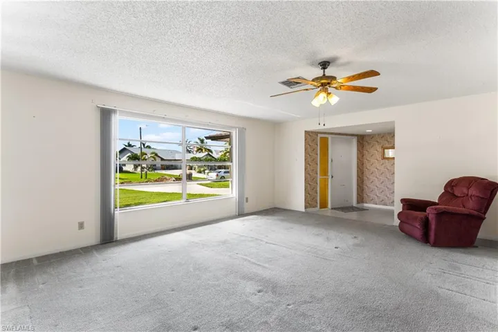 Unfurnished living room with a textured ceiling, carpet floors, and ceiling fan