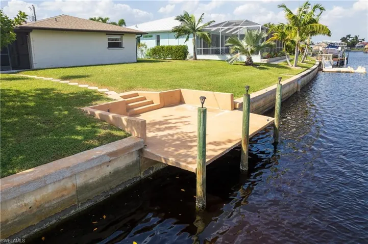 View of dock with glass enclosure, a water view, and a lawn