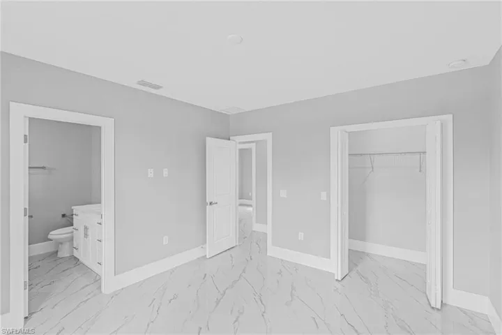 Spacious room featuring large format tile flooring, a walk-in closet with wire shelving, and a bright white interior door leading to a bathroom with a vanity and toilet