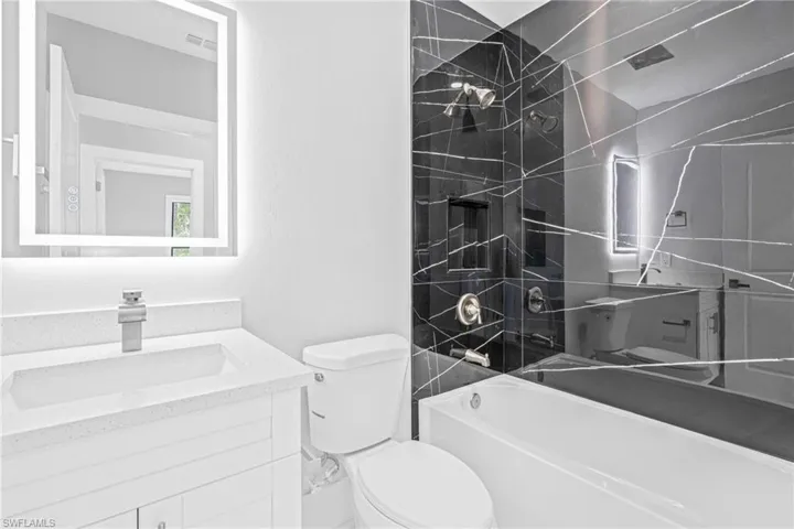 Bathroom featuring a modern vanity with quartz countertop, a backlit mirror, and brushed nickel fixtures