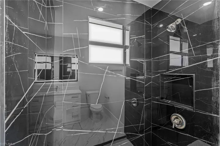 Bathroom featuring a glass-enclosed shower with black marble-finish tile, integrated shower niche, and a chrome shower head