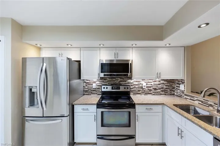 Kitchen featuring appliances with stainless steel finishes, white cabinetry, light stone counters, recessed lighting, and decorative backsplash