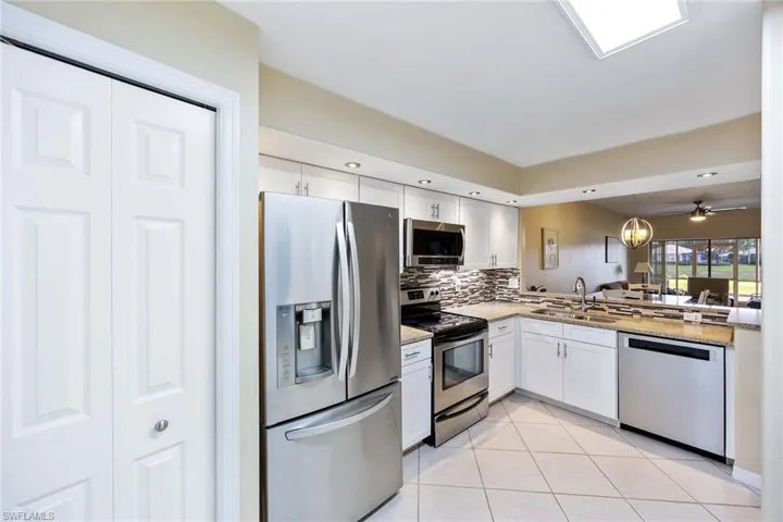 Kitchen with stainless steel appliances, white cabinetry, decorative light fixtures, light stone counters, and light tile patterned floors