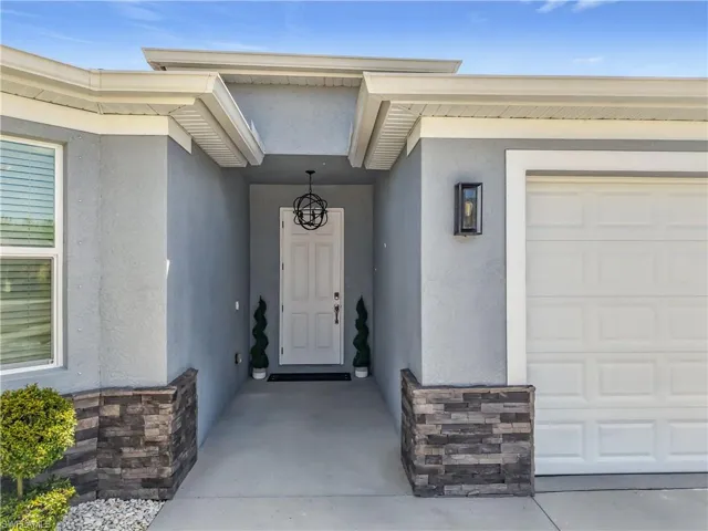 Entrance to property with an attached garage, stone siding, and stucco siding