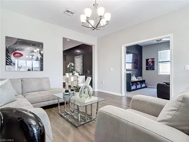 Living area featuring baseboards, a notable chandelier, visible vents, and wood finished floors