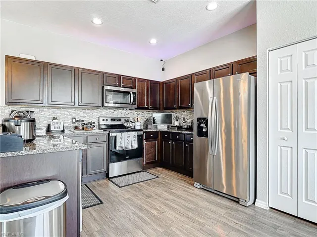 Kitchen with light wood-style flooring, appliances with stainless steel finishes, dark brown cabinets, and backsplash