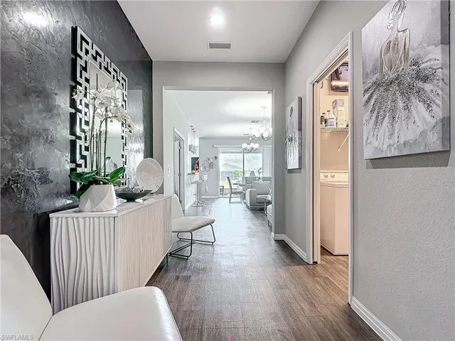 Hallway with a notable chandelier, visible vents, a textured wall, wood finished floors, and baseboards