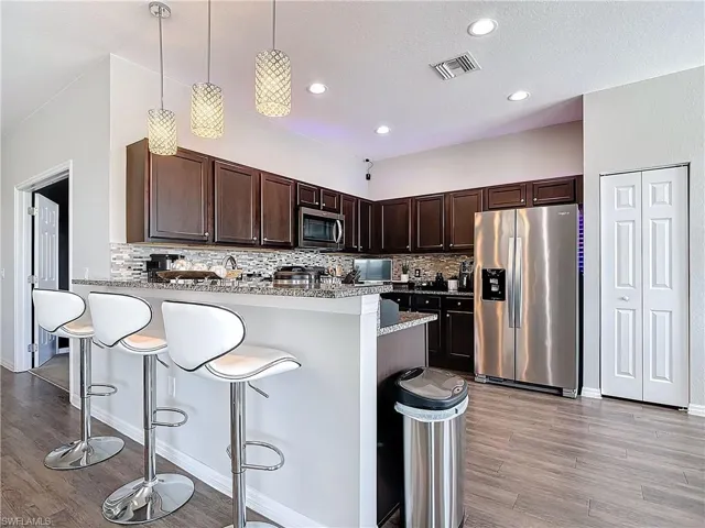 Kitchen featuring dark brown cabinetry, visible vents, a peninsula, stainless steel appliances, and a kitchen bar