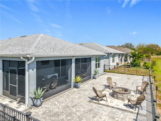 Rear view of property featuring a sunroom, a shingled roof, an outdoor fire pit, and a patio
