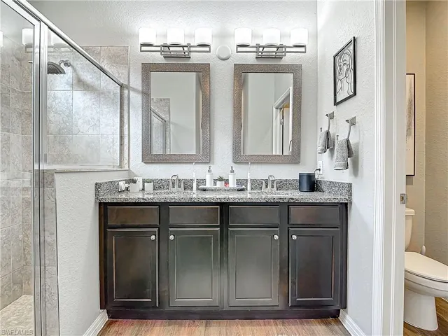 Full bathroom with double vanity, toilet, a stall shower, a sink, and wood finished floors