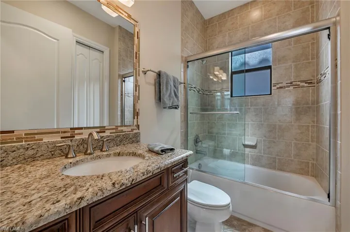Guest bathroom #3 featuring toilet, vanity, and bath / shower combo with glass door