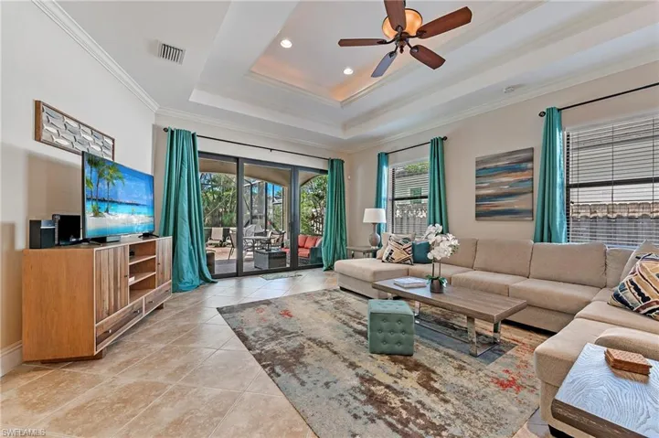 Great Room with crown molding, porcelain tiled flooring, ceiling fan, and a tray ceiling