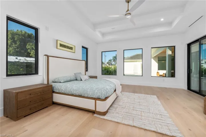 Bedroom with light wood-type flooring, a tray ceiling, recessed lighting, baseboards, and ceiling fan