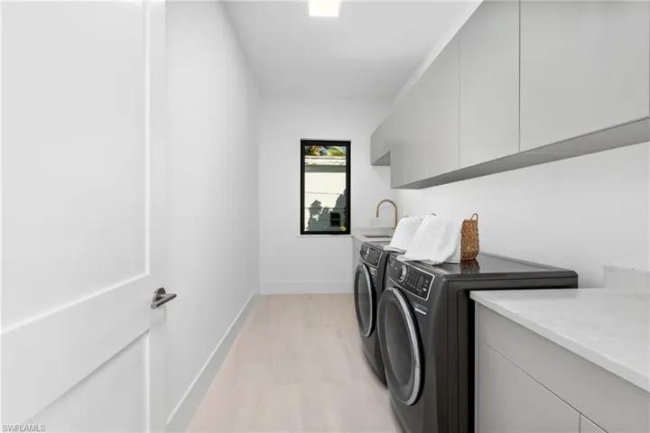 Laundry area with baseboards, separate washer and dryer, cabinet space, a sink, and light wood-style floors