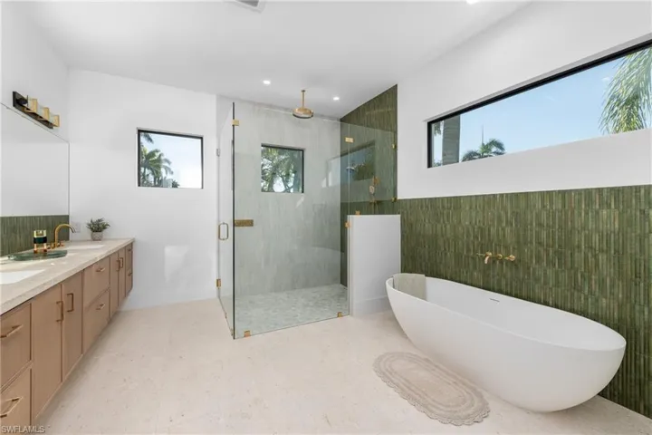 Bathroom with double vanity, a stall shower, a soaking tub, tile walls, and a sink