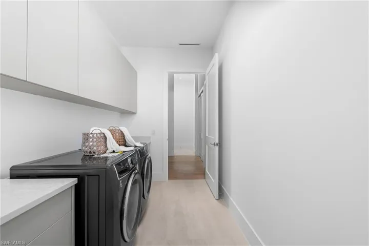 Laundry area with washing machine and clothes dryer, visible vents, baseboards, light wood-style floors, and cabinet space