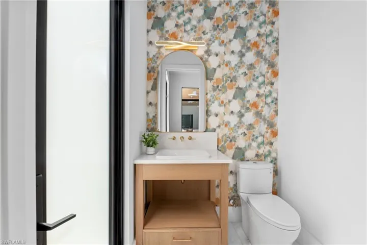 Half bath featuring toilet, wallpapered walls, and vanity