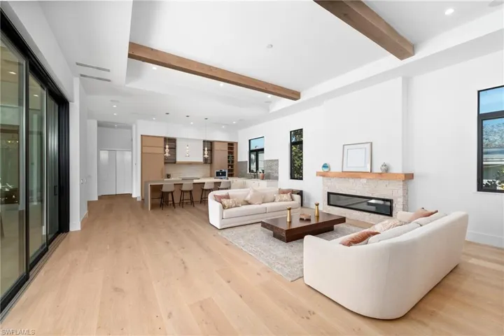 Living area featuring beam ceiling, recessed lighting, a stone fireplace, light wood finished floors, and baseboards