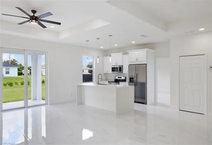 Open-concept living space with sleek tile flooring, a modern kitchen island, white cabinetry, and stainless steel appliances