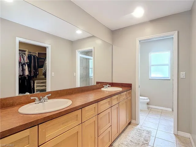 Bathroom with vanity, with dual sinks, tile flooring, enclosed toilet, and  shower with door