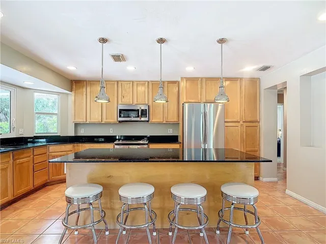 Kitchen featuring wood cabinetry, granite counters, stainless appliances and pendant lighting, a kitchen bar, appliances with stainless steel finishes, and a kitchen island