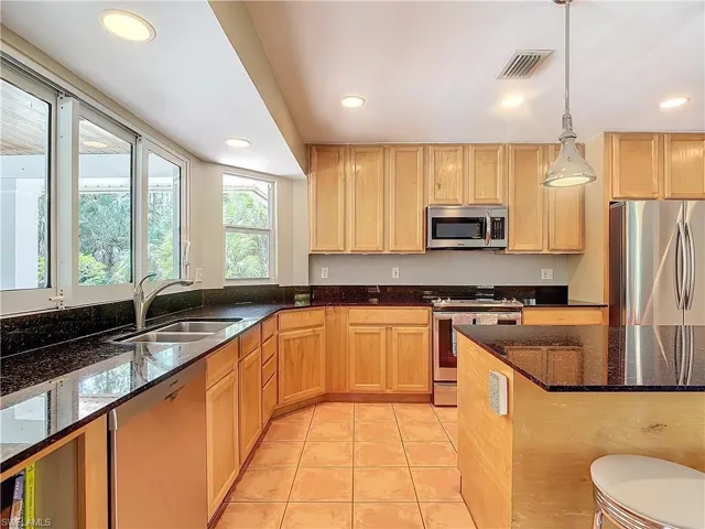 Kitchen featuring newer appliances with stainless steel finishes, recessed and pendant light fixtures, tile patterned floors, dark granite counters, and stainless sink.