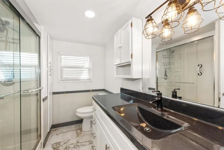 Bathroom with vanity, a stall shower, light marble finish floors, a wainscoted wall, and a chandelier
