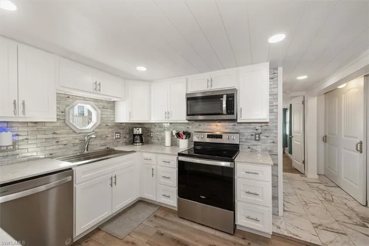 Kitchen featuring stainless steel appliances, white cabinets, recessed lighting, light stone countertops, and tasteful backsplash