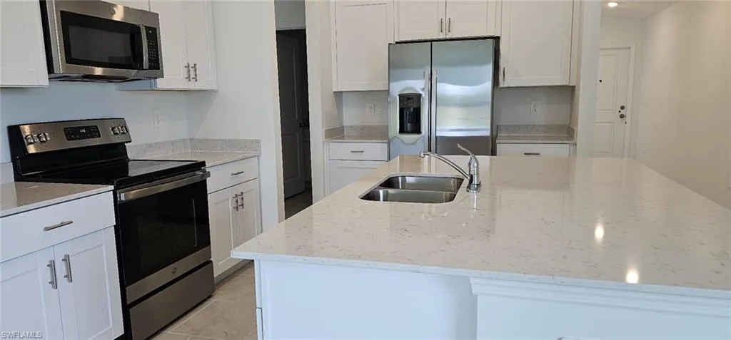 Kitchen featuring stainless steel appliances, white cabinets, and light stone countertops