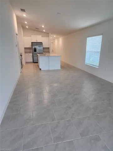 Kitchen with white cabinets, lofted ceiling, a center island with sink, stainless steel fridge, and open floor plan