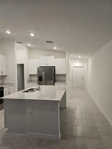 Kitchen with white cabinetry, stainless steel appliances, vaulted ceiling, light stone countertops, and a kitchen island with sink