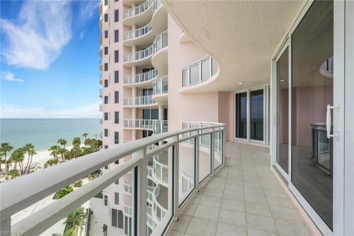 Expansive balcony featuring tiled flooring, a glass and metal railing, and multiple sliding glass doors