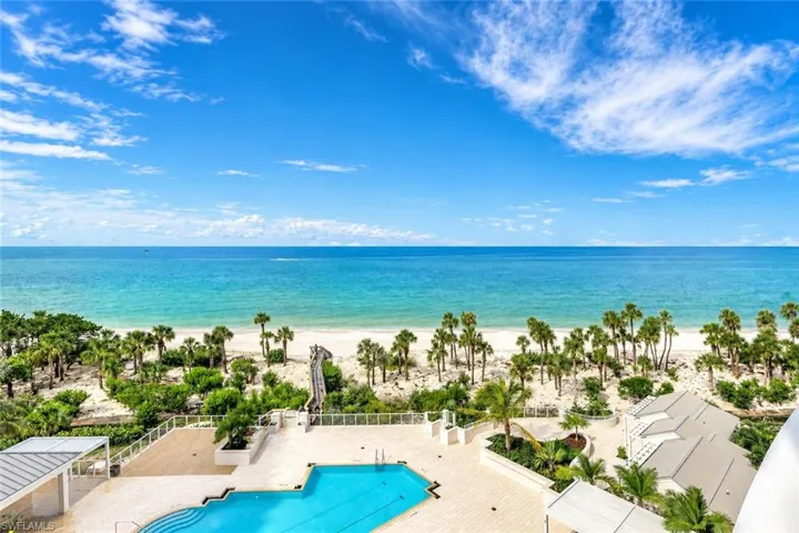 Expansive turquoise ocean, sandy beach, palm trees, outdoor swimming pool, and a poolside deck