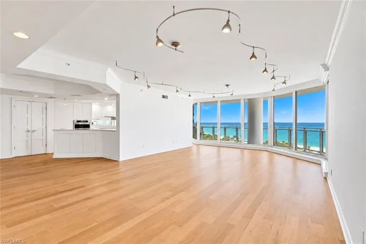 Curved floor-to-ceiling windows, light wood-finish flooring, white built-in cabinetry, modern track lighting, and recessed ceiling lights