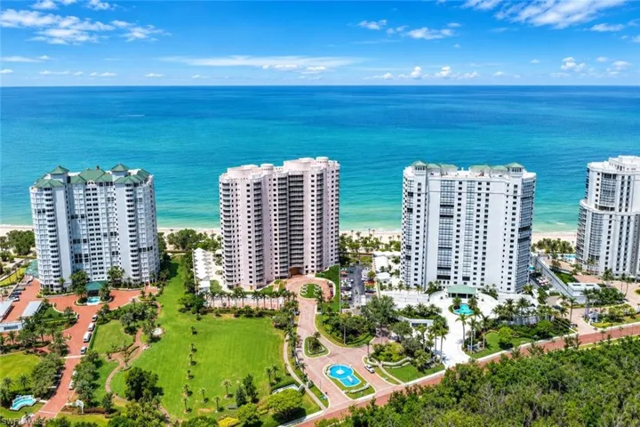 Coastal setting with multiple high-rise buildings, extensive green spaces, a beachfront, and a prominent water feature at the entry
