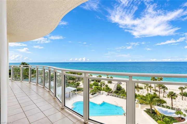 Expansive curved balcony featuring a glass railing, tiled flooring, and direct beachfront access