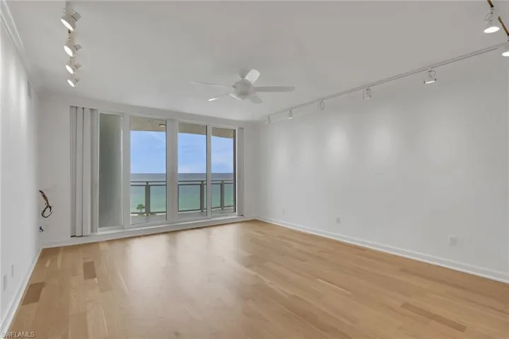 Full-height glass panels with balcony access, wood-finish flooring, ceiling fan, and track lighting fixtures