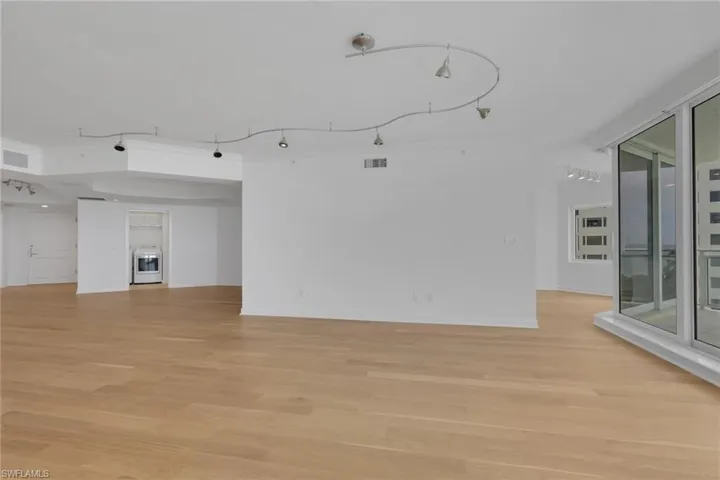 Expansive open living space with wood-finish flooring, white walls, track lighting, and floor-to-ceiling windows