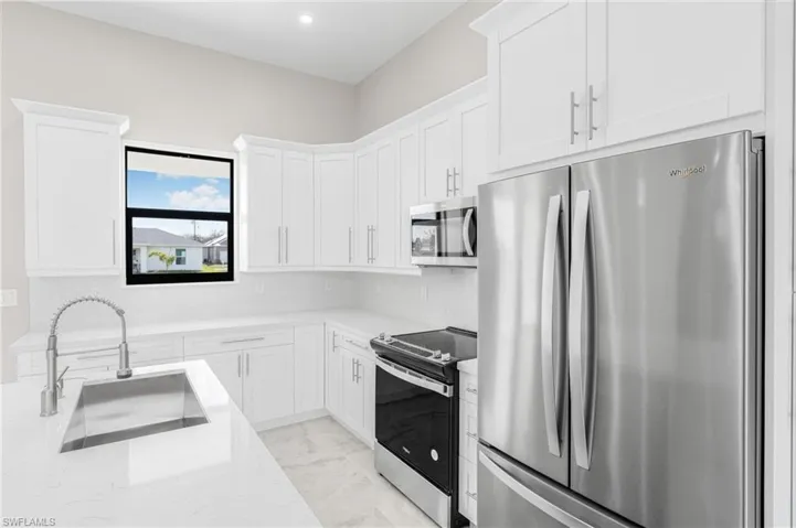 Kitchen with white cabinetry, sink, light stone counters, and appliances with stainless steel finishes