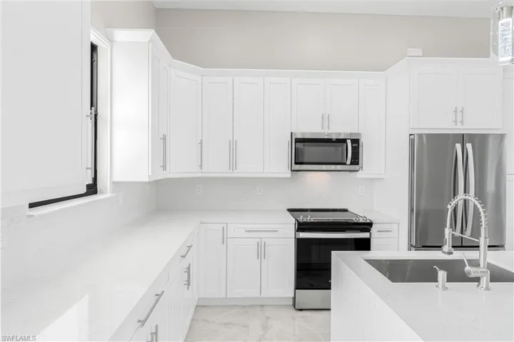 Kitchen featuring light stone counters, sink, white cabinets, and appliances with stainless steel finishes