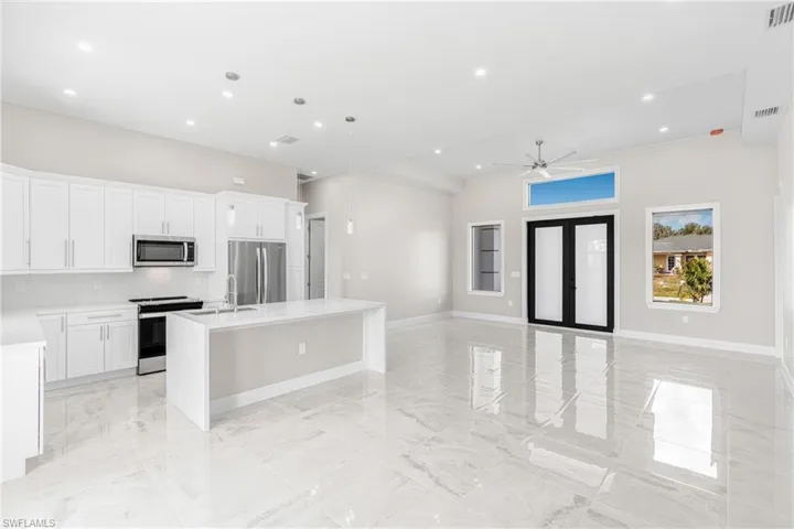 Kitchen with stainless steel appliances, tasteful backsplash, white cabinets, a center island with sink, and decorative light fixtures