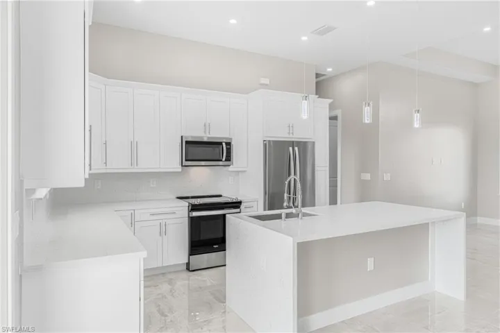 Kitchen with appliances with stainless steel finishes, pendant lighting, an island with sink, sink, and white cabinets