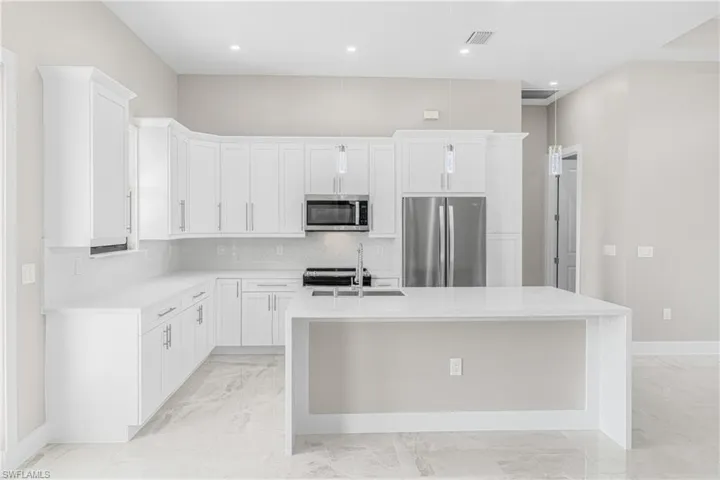 Kitchen with stainless steel appliances, white cabinetry, sink, and a center island with sink