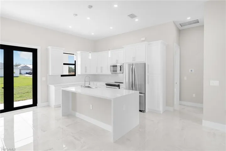 Kitchen with sink, appliances with stainless steel finishes, pendant lighting, a kitchen island with sink, and white cabinets